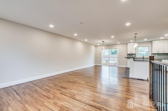 unfurnished living room with light wood finished floors, a sink, recessed lighting, a chandelier, and baseboards
