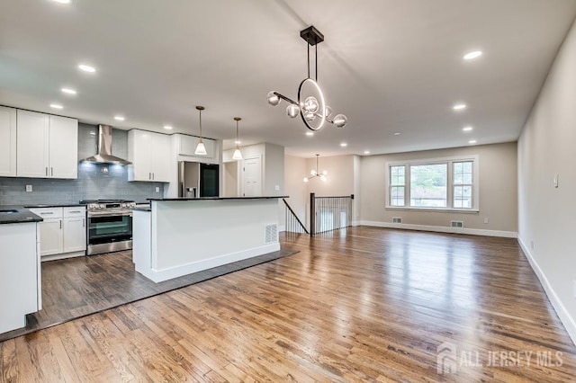 kitchen featuring appliances with stainless steel finishes, wall chimney exhaust hood, dark countertops, a chandelier, and wood finished floors