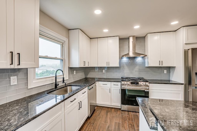 kitchen with wall chimney range hood, stainless steel appliances, a sink, white cabinetry, and recessed lighting