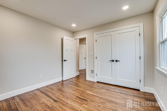 unfurnished bedroom featuring baseboards, light wood finished floors, recessed lighting, and multiple windows