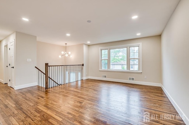 empty room with a chandelier, wood finished floors, baseboards, and recessed lighting