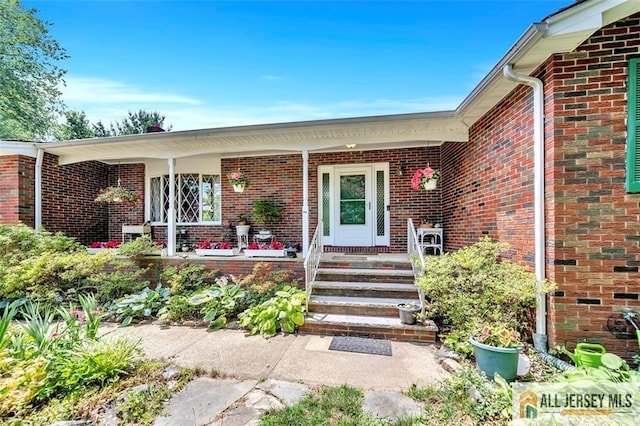 view of exterior entry featuring brick siding and covered porch