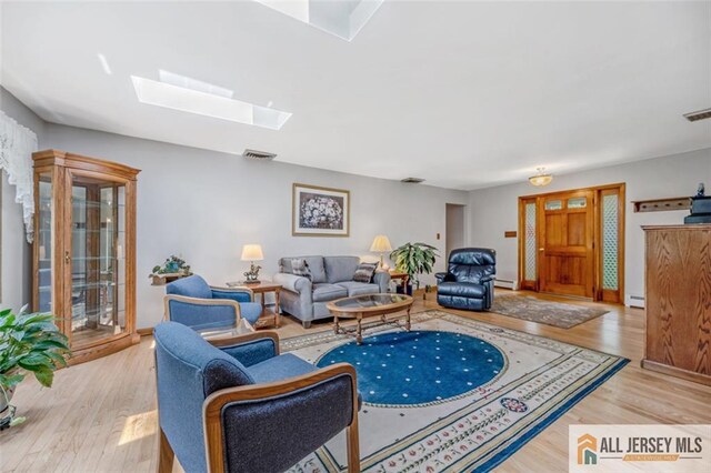 living room featuring light wood-type flooring, a skylight, and a baseboard heating unit