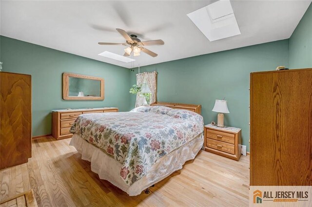 bedroom with ceiling fan, a skylight, and light hardwood / wood-style floors