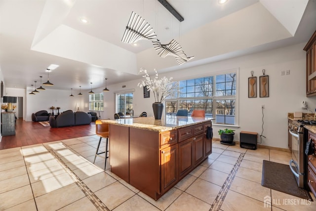 kitchen featuring a kitchen bar, a tray ceiling, decorative light fixtures, stainless steel range oven, and a center island