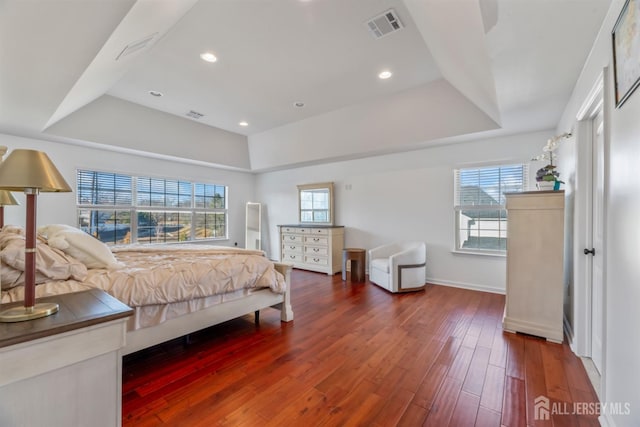 bedroom featuring multiple windows, dark hardwood / wood-style flooring, and a raised ceiling