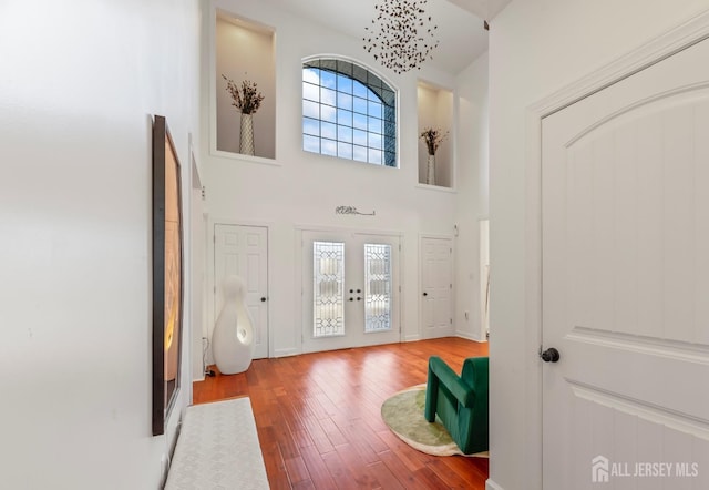 entrance foyer with hardwood / wood-style flooring, a high ceiling, french doors, and a notable chandelier