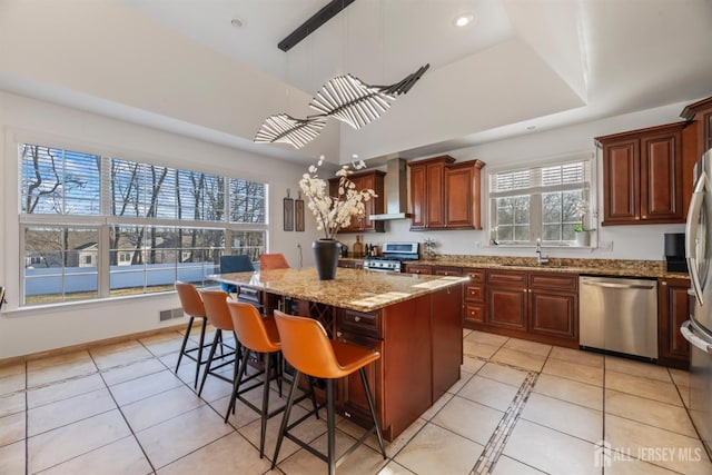 kitchen featuring a kitchen island, wall chimney range hood, stainless steel appliances, sink, and light tile patterned flooring