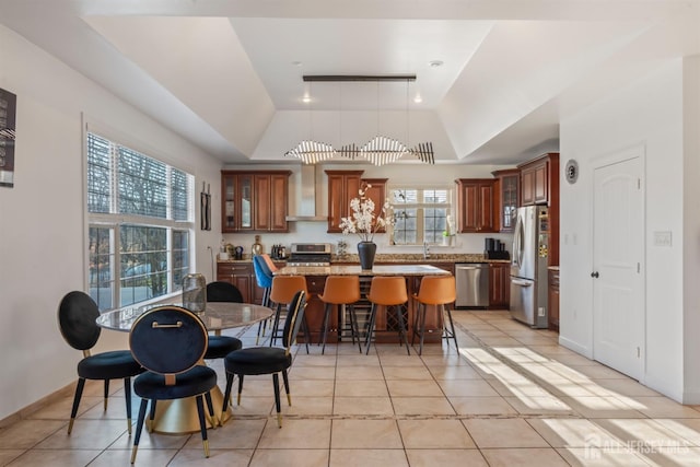 kitchen with wall chimney range hood, appliances with stainless steel finishes, a center island, and a healthy amount of sunlight