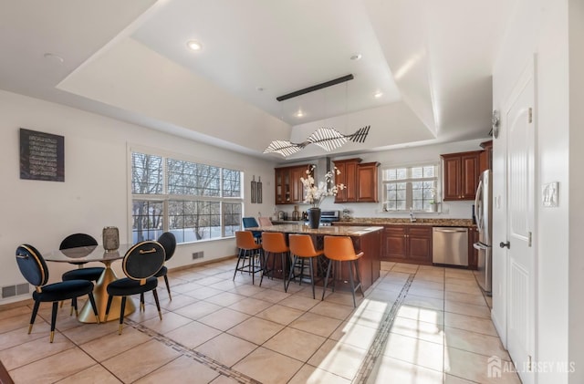 kitchen with decorative light fixtures, a center island, a raised ceiling, stainless steel appliances, and light tile patterned floors