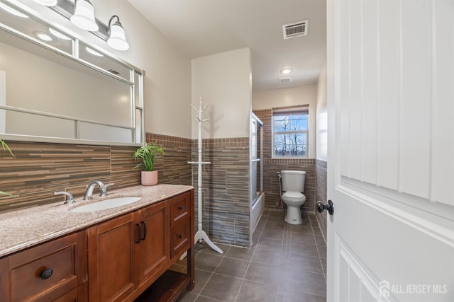 bathroom featuring toilet, vanity, tile patterned flooring, tile walls, and walk in shower