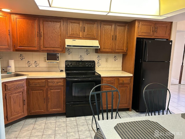 kitchen featuring backsplash, ventilation hood, black appliances, and light countertops