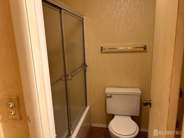 bathroom with tile patterned flooring, toilet, baseboards, and shower / bath combination with glass door