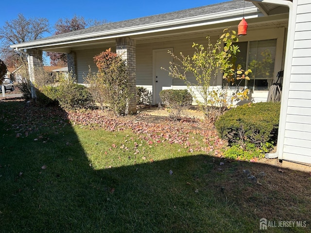 view of side of property featuring brick siding, a shingled roof, and a yard