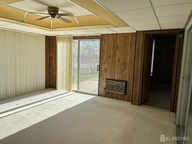 empty room featuring a ceiling fan, wooden walls, a fireplace, carpet flooring, and a paneled ceiling