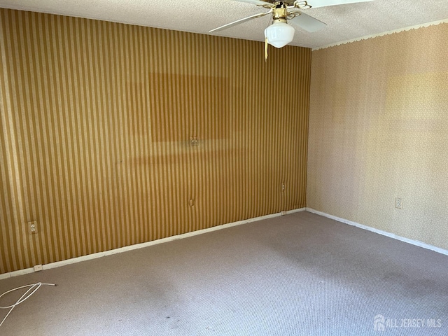 carpeted spare room with wallpapered walls, a ceiling fan, baseboards, and a textured ceiling