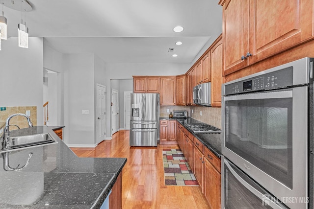 kitchen featuring decorative backsplash, light wood-style flooring, appliances with stainless steel finishes, dark stone countertops, and a sink