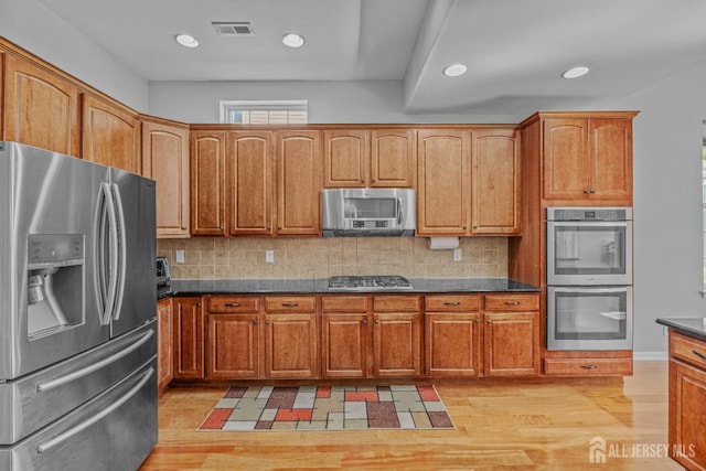 kitchen featuring appliances with stainless steel finishes, light wood-style floors, visible vents, and decorative backsplash