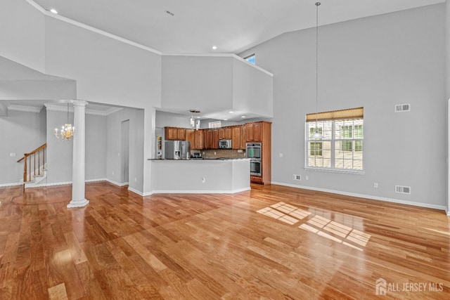 unfurnished living room featuring crown molding, light wood-style floors, decorative columns, and a notable chandelier