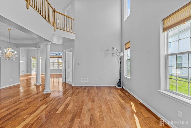 unfurnished living room featuring ornate columns, visible vents, an inviting chandelier, wood finished floors, and baseboards