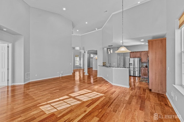 unfurnished living room featuring a high ceiling, visible vents, light wood-type flooring, ornate columns, and crown molding