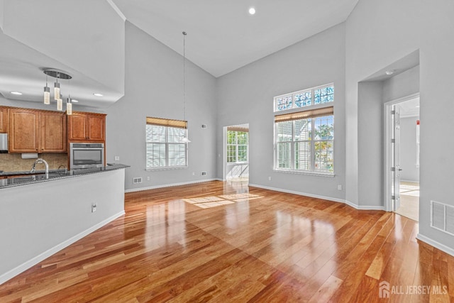 unfurnished living room featuring light wood finished floors, a towering ceiling, visible vents, and baseboards