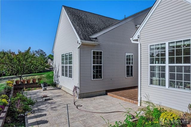 view of side of property featuring a shingled roof and a patio area