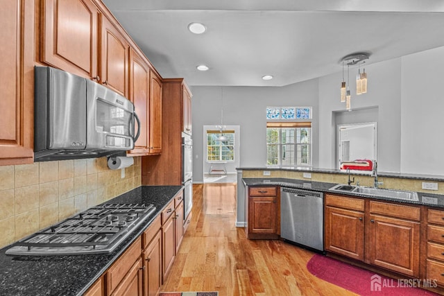 kitchen with stainless steel appliances, a sink, light wood-style floors, backsplash, and brown cabinetry