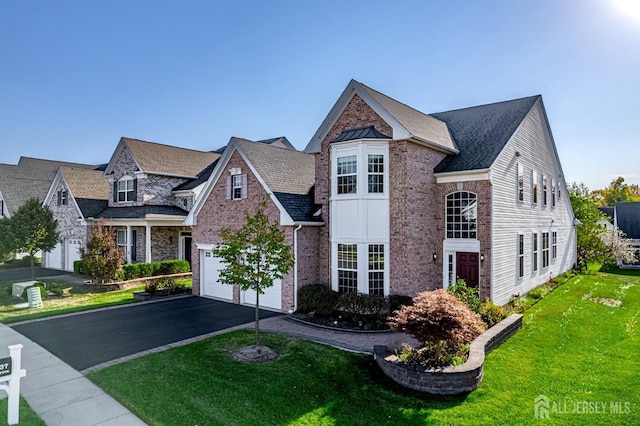 traditional-style home with driveway, brick siding, a front yard, and a shingled roof