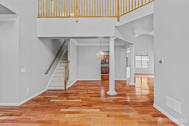 unfurnished living room with a high ceiling, wood finished floors, visible vents, stairway, and ornate columns