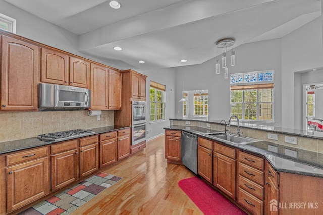 kitchen featuring stainless steel appliances, decorative backsplash, light wood-style floors, a healthy amount of sunlight, and a sink