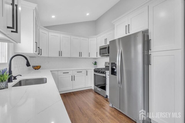 kitchen with light stone countertops, appliances with stainless steel finishes, white cabinetry, dark hardwood / wood-style flooring, and sink