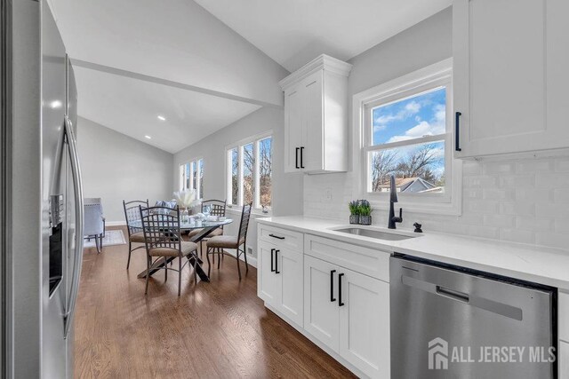 kitchen featuring appliances with stainless steel finishes, decorative backsplash, lofted ceiling, white cabinets, and sink