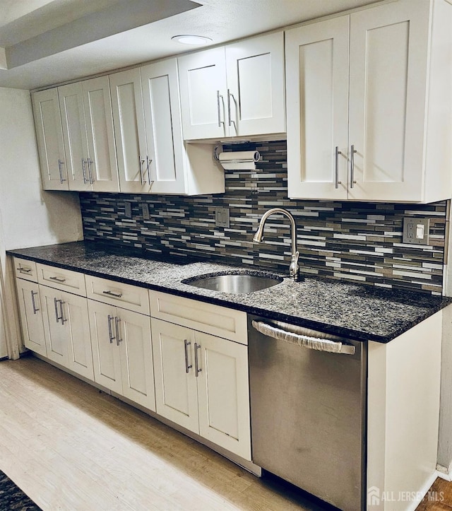 kitchen with a sink, light wood-type flooring, white cabinetry, stainless steel dishwasher, and decorative backsplash