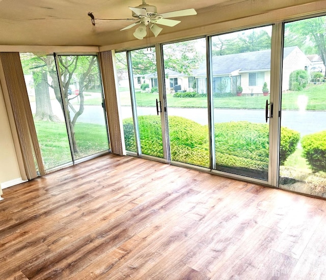 unfurnished sunroom with ceiling fan, a water view, and wood finished floors