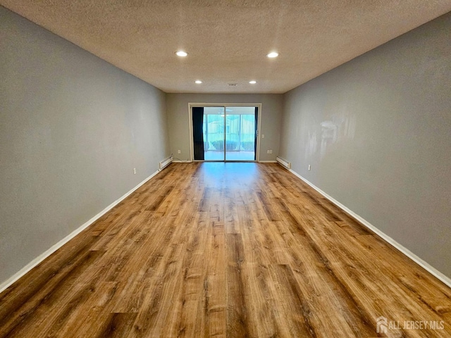 empty room featuring wood finished floors, recessed lighting, baseboards, a textured ceiling, and a baseboard heating unit