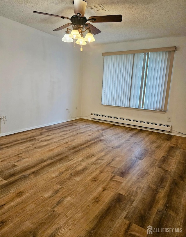 empty room featuring wood finished floors, a textured ceiling, visible vents, baseboard heating, and ceiling fan