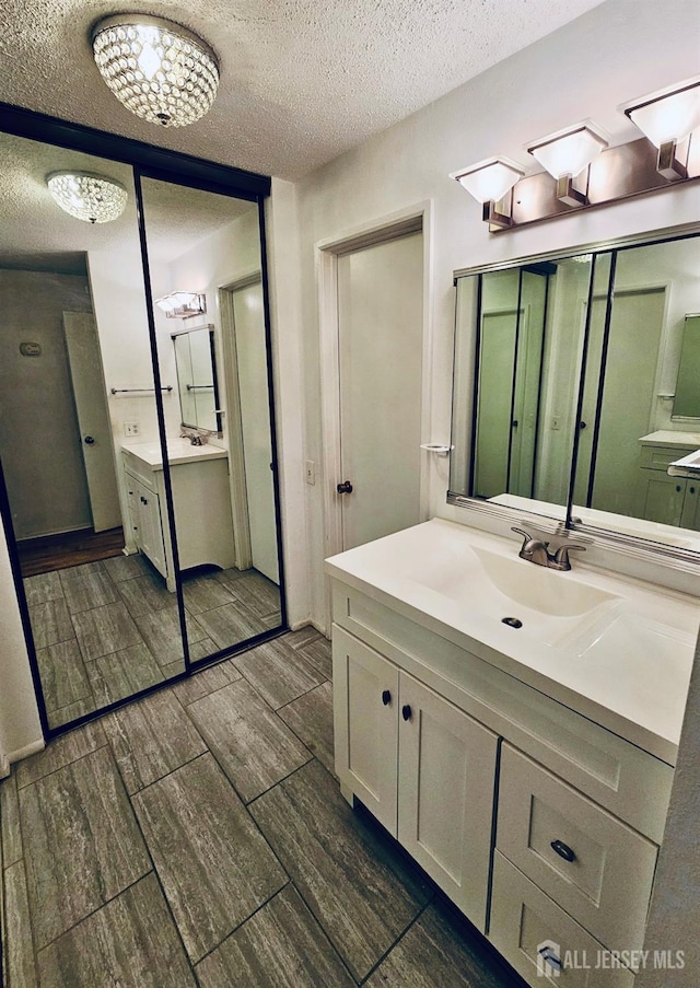 bathroom with a textured ceiling, wood tiled floors, and two vanities