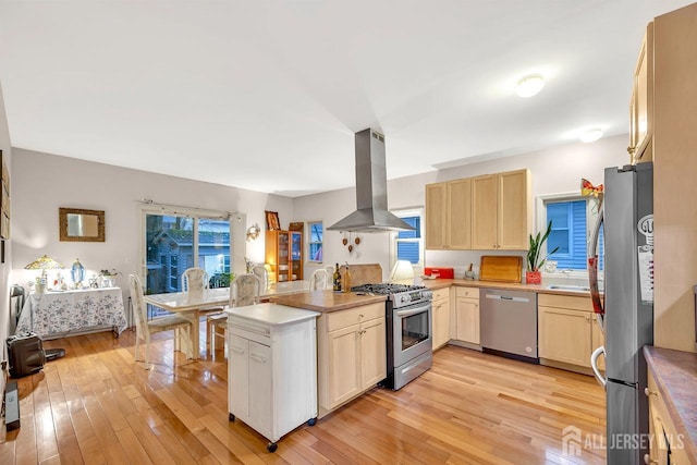 kitchen with a peninsula, appliances with stainless steel finishes, island exhaust hood, and light wood-style floors