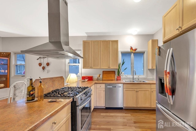 kitchen with island exhaust hood, light wood finished floors, light brown cabinetry, appliances with stainless steel finishes, and a sink