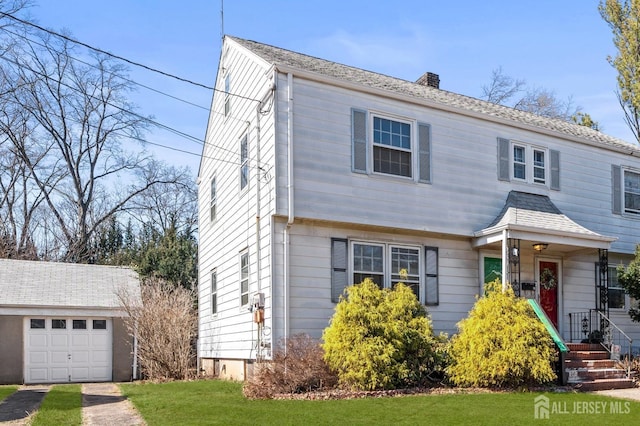 colonial-style house featuring an outbuilding, a front yard, a shingled roof, a garage, and a chimney