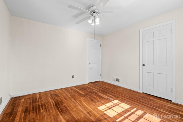 empty room featuring a ceiling fan, wood finished floors, visible vents, and baseboards