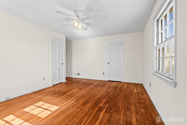 empty room featuring hardwood / wood-style floors, visible vents, a ceiling fan, and baseboards