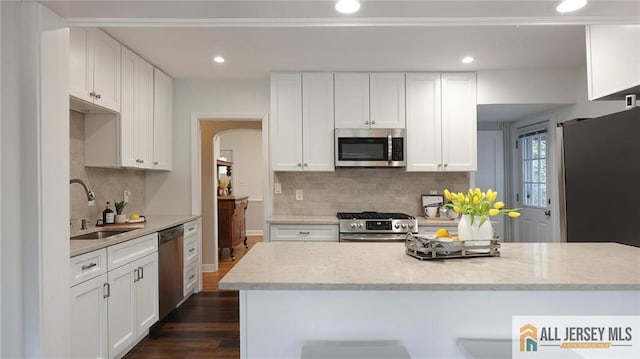 kitchen featuring arched walkways, a sink, appliances with stainless steel finishes, dark wood-type flooring, and decorative backsplash