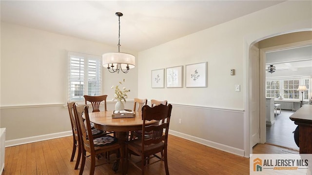 dining area with hardwood / wood-style floors, a notable chandelier, baseboards, and arched walkways