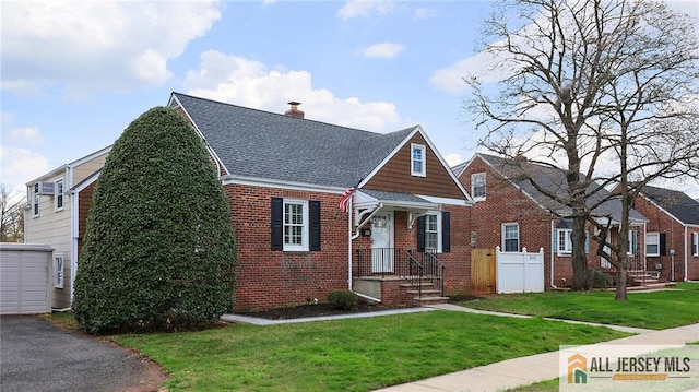 view of front of house featuring a shingled roof, a front yard, fence, and brick siding