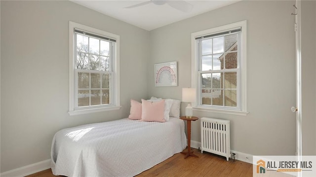 bedroom with baseboards, a ceiling fan, radiator, and wood finished floors