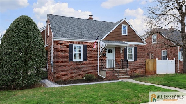 view of front of house featuring a shingled roof, fence, a front lawn, and brick siding