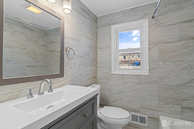 bathroom with toilet, vanity, visible vents, and tile walls