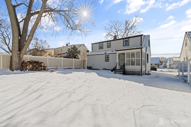 snow covered rear of property with entry steps, a chimney, fence, and a sunroom